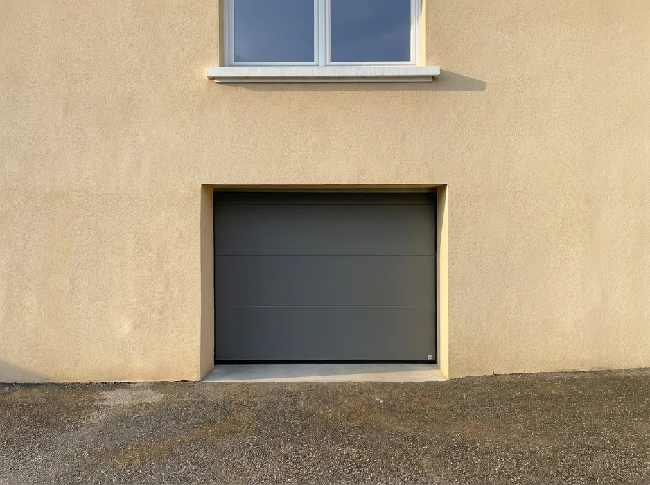 Façade extérieure d'une maison en enduit beige avec une porte de garage sectionnelle, coloris gris anthracite RAL 7016, finition lisse