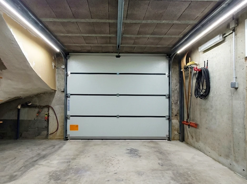 Garage en sous-sol béton apparent, porte sectionnelle automatique blanche 4 panneaux avec rails latéraux et motorisation centrale