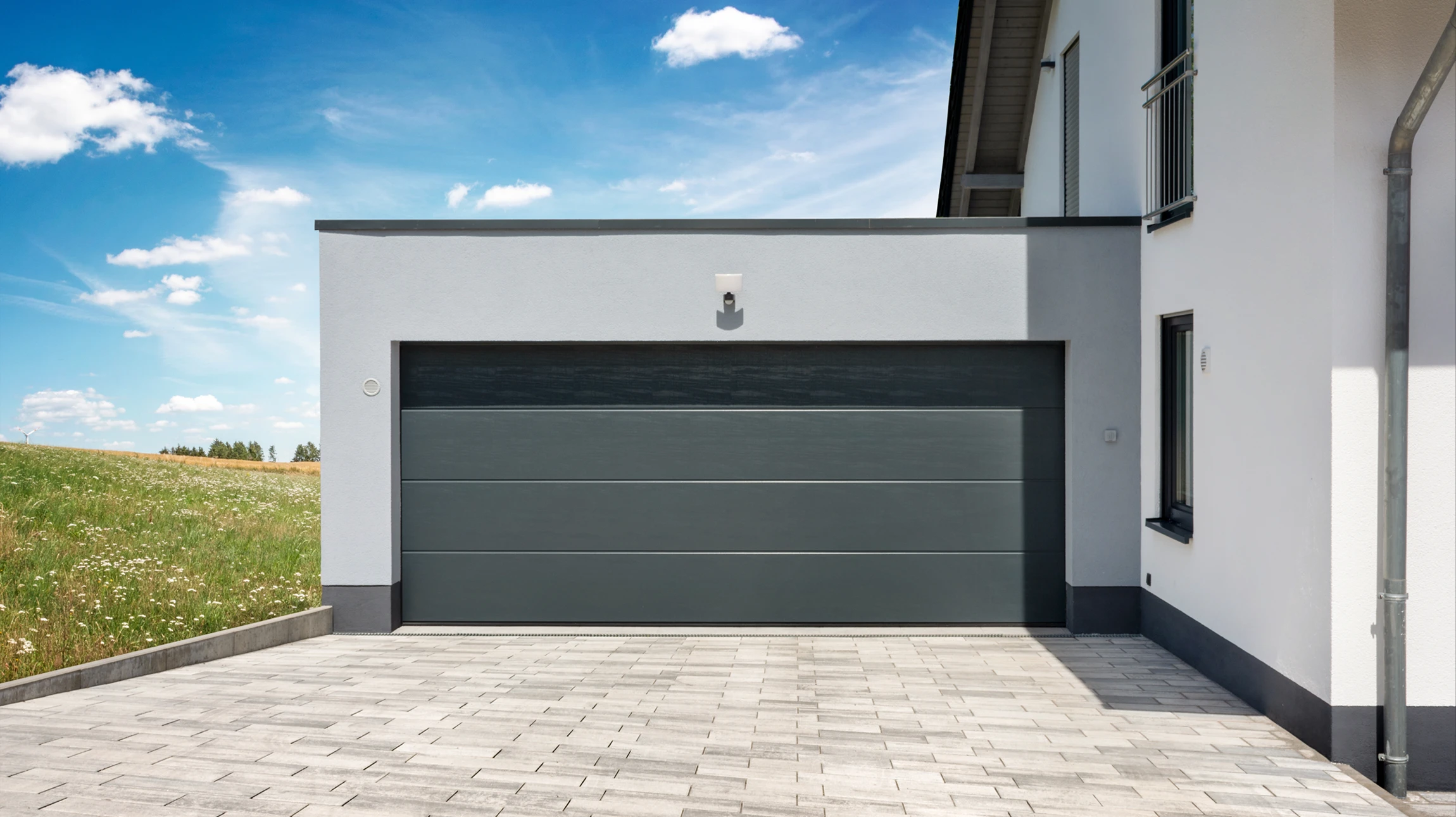 Artisan professionnel en tenue de travail installant ou remplaçant une porte de garage résidentielle. L'image montre la porte de garage en cours de mise en place ou de maintenance, avec l'artisan effectuant son travail d'installation. Arrière-plan : façade d'habitation. Photo professionnelle en lumière naturelle.