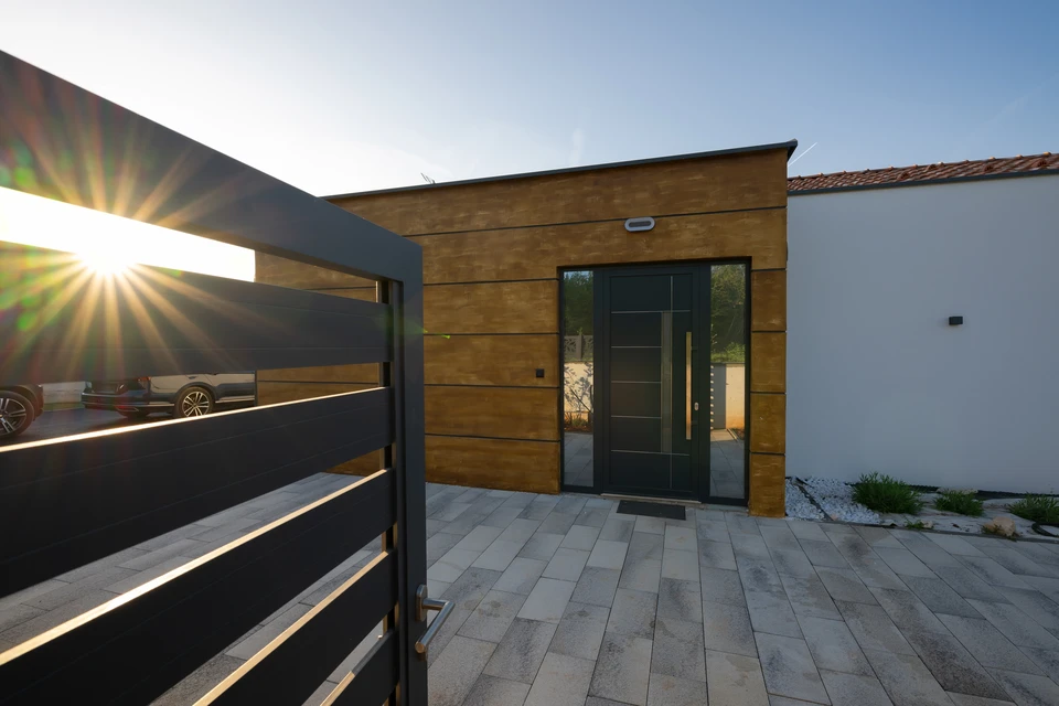Scène extérieure résidentielle avec clôture moderne en aluminium noir à barreaux verticaux longeant une pelouse verte bien entretenue