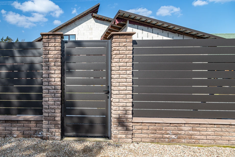 Scène extérieure résidentielle avec clôture moderne en aluminium noir à barreaux verticaux longeant une pelouse verte bien entretenue