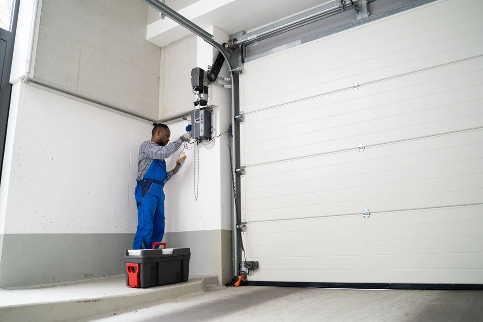 Un artisan menuisier expérimenté guidant un poseur plus jeune lors de l'installation d'une fenêtre ou d'une porte d'entrée. Les deux hommes sont concentrés sur le travail, l'un montrant à l'autre les détails techniques d'ajustement ou de pose. La scène se déroule sur un chantier réel de rénovation, avec des matériaux de qualité visibles. L'image doit transmettre le professionnalisme, la transmission de compétences et la confiance mutuellement établie.