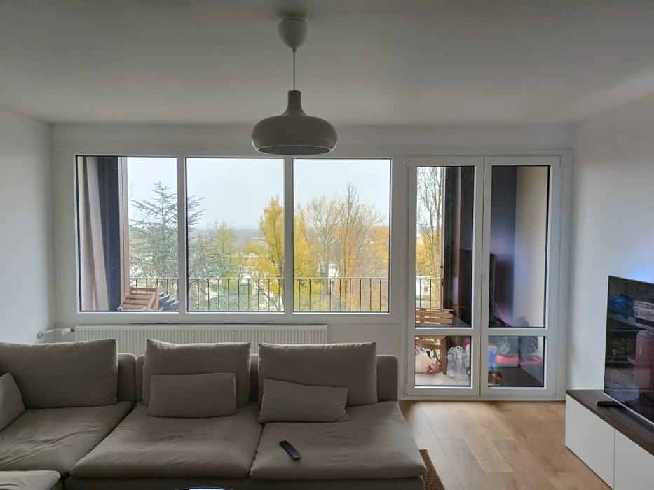 Porte-fenêtre coulissante en PVC blanc vue depuis l'extérieur, donnant sur une salle à manger avec chaise haute bébé et table à manger