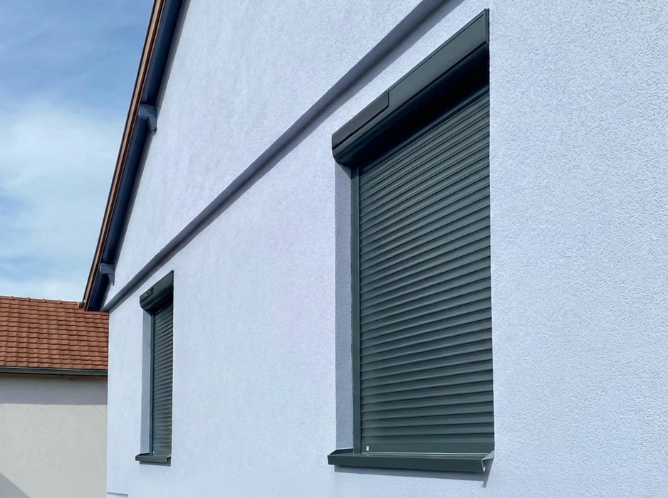 Façade extérieure en crépi beige avec fenêtre équipée d'un volet roulant métallique fermé, coloris sable