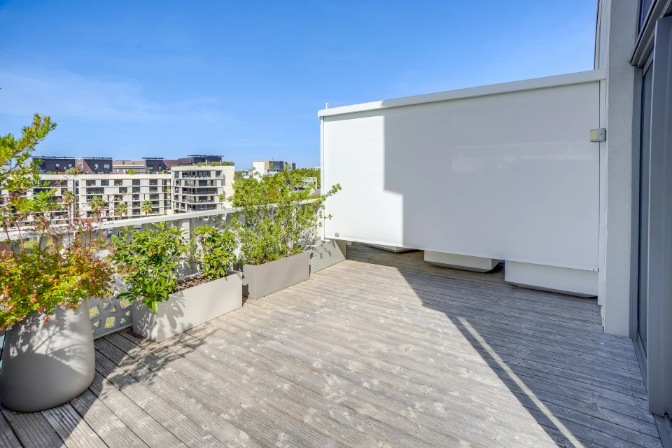 Intérieur d'un salon donnant sur une terrasse couverte via une baie vitrée coulissante double vantaux à cadre PVC blanc