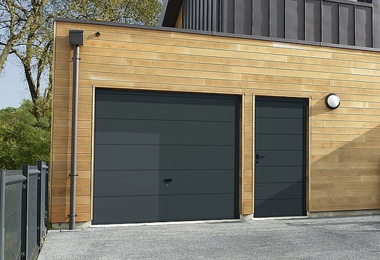 Garage moderne à deux portes sectionnelles coulissantes en lamelles métalliques anthracite intégrées dans façade contemporaine blanche