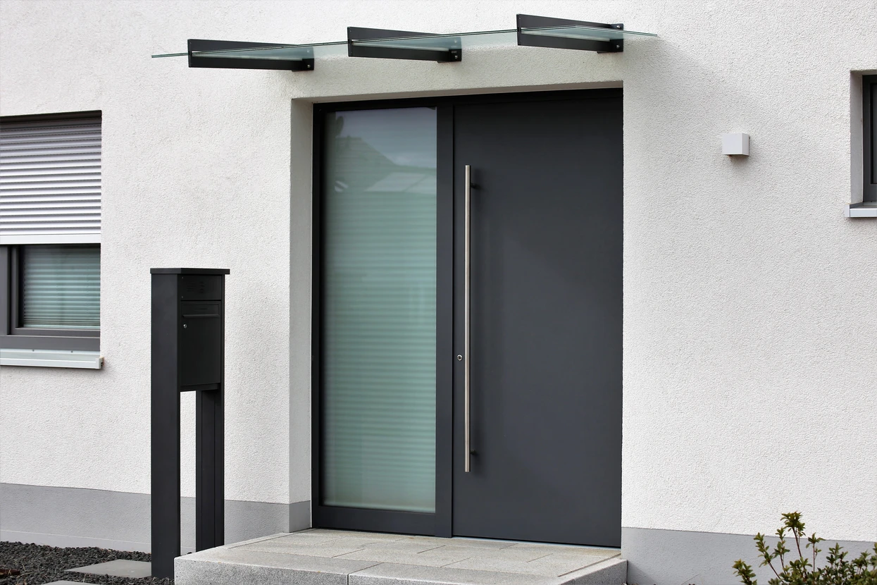 Entrée extérieure de maison moderne avec porte d'entrée contemporaine noire à panneau vitré supérieur et poignée métallique dorée